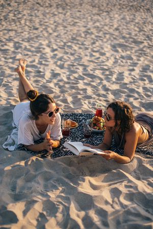 Two women enjoying a relaxing beach picnic with drinks and snacks in Vietnam.