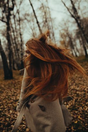Woman with flowing red hair walks through autumn forest, adding dynamic movement to the scene.