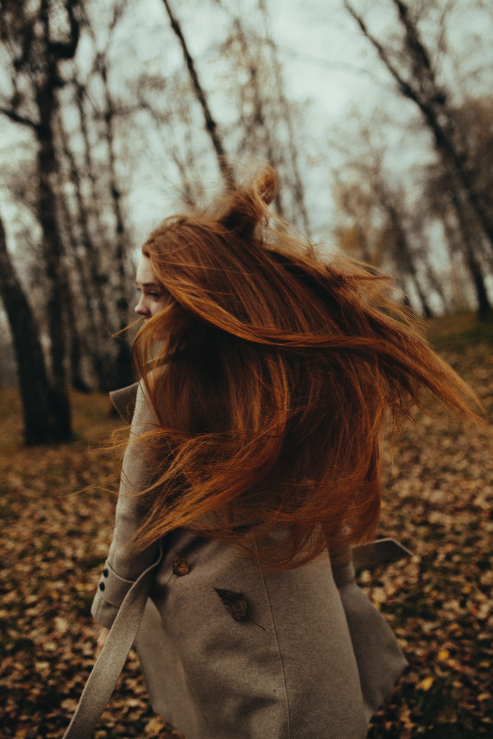 Woman with flowing red hair walks through autumn forest, adding dynamic movement to the scene.